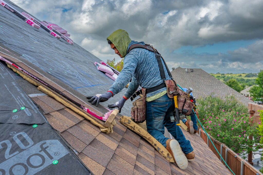 Roofers installing asphalt shingles on a home's roof under a blue sky
