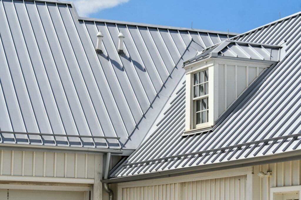 Grey standing seam metal roof with a dormer window over white siding